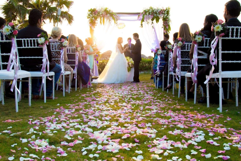 A wedding couple holding hands in a destination wedding surrounded by the guests and flower decor